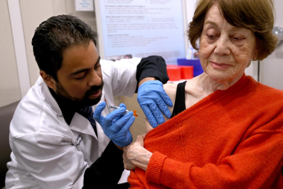 A doctor gives a vaccine to a woman wearing a red sweater. 