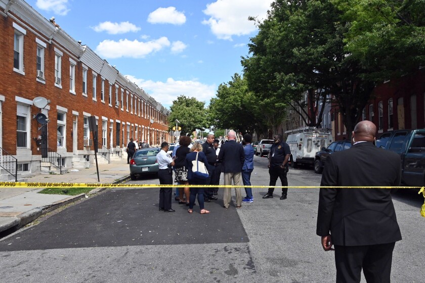 Baltimore Police Commissioner Michael Harrison, center, Baltimore Mayor Brandon Scott, second from right, confer at the scene of a shooting, Wednesday, June 16, 2021, in Baltimore. One person was killed and five others were wounded Wednesday when gunmen walked up a street and opened fire on a Baltimore block from an intersection, the city's police commissioner said. (Kim Hairston/The Baltimore Sun via AP)