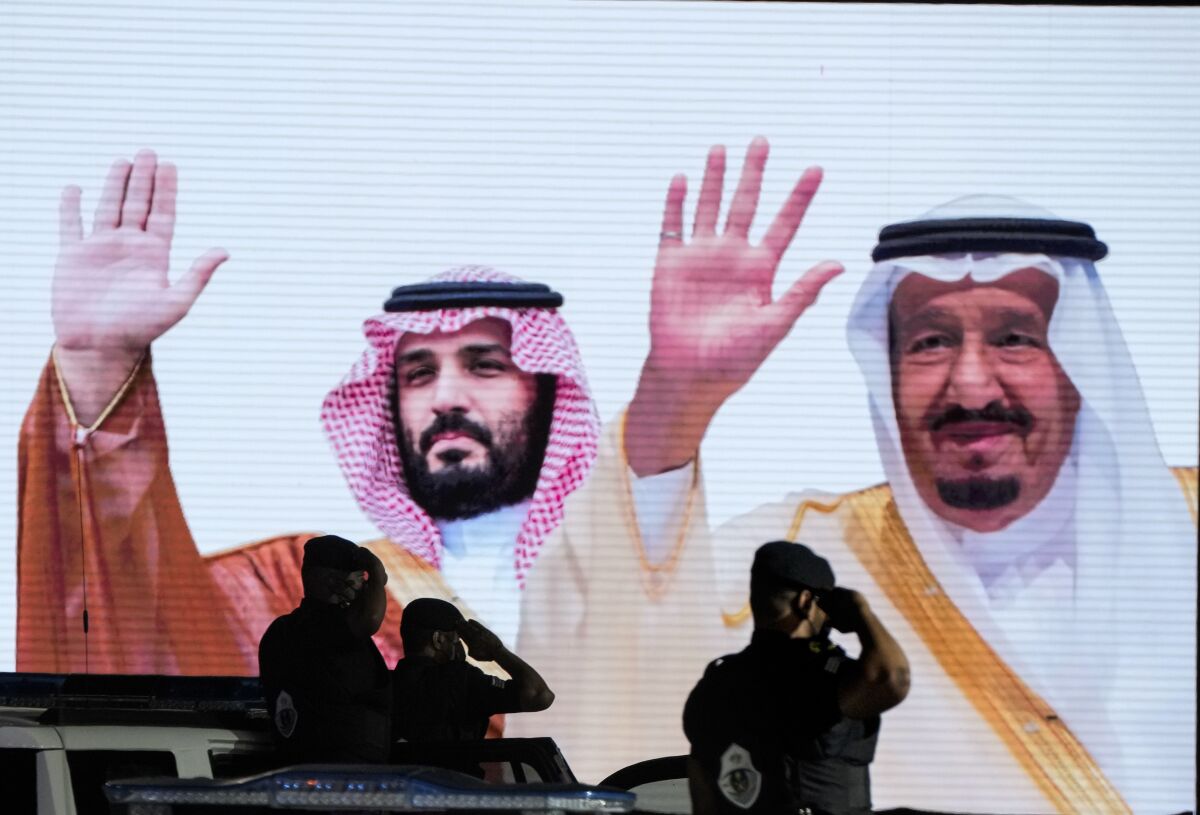 Saudi special forces salute in front of a screen displaying images Saudi King Salman and Crown Prince Mohammed bin Salman
