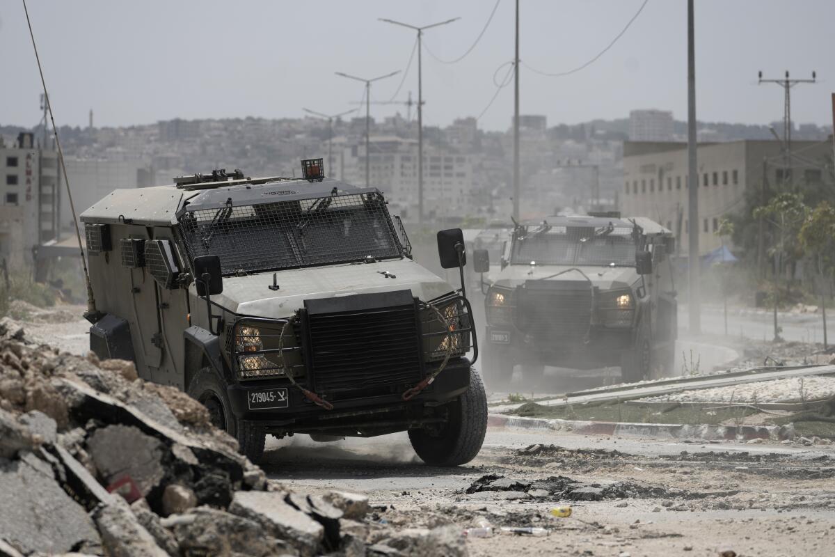 Israeli military vehicles navigate through a rubble-strewn road in Jenin, West Bank