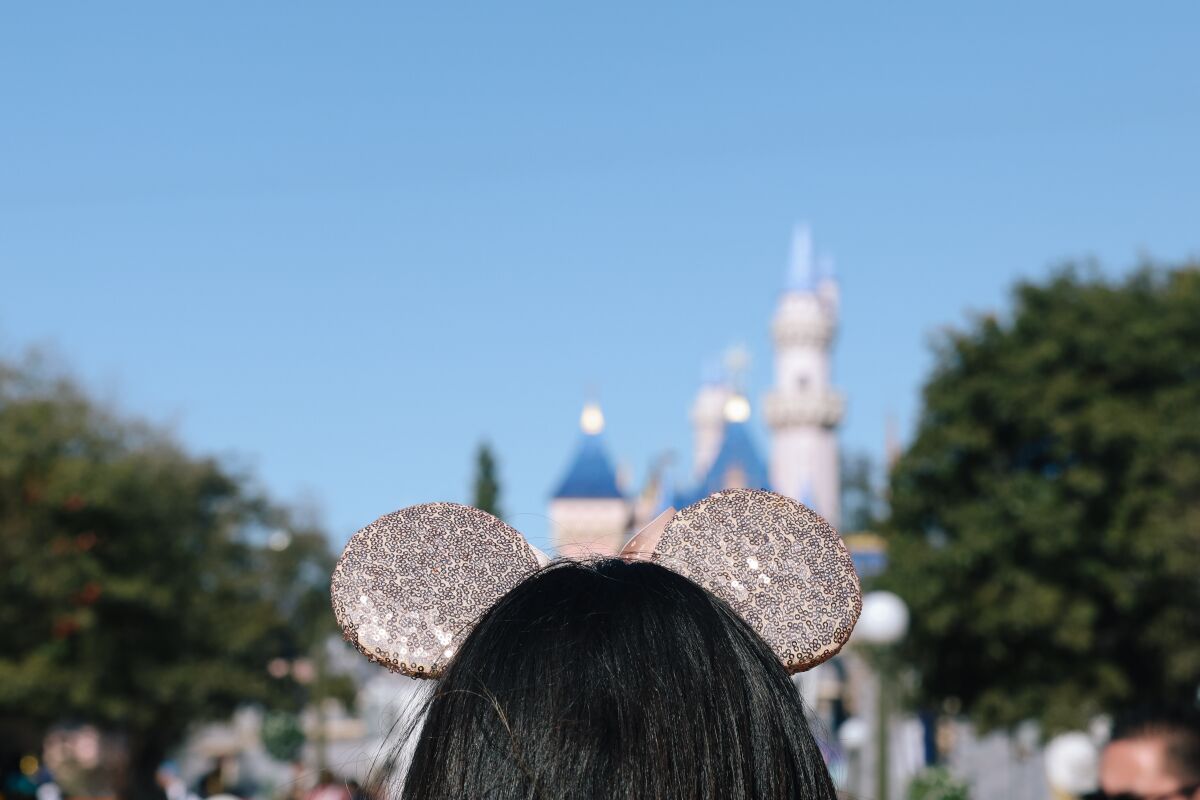 The back of a person's head wearing glittery mouse ears with an out-of-focus Disneyland castle in the background.