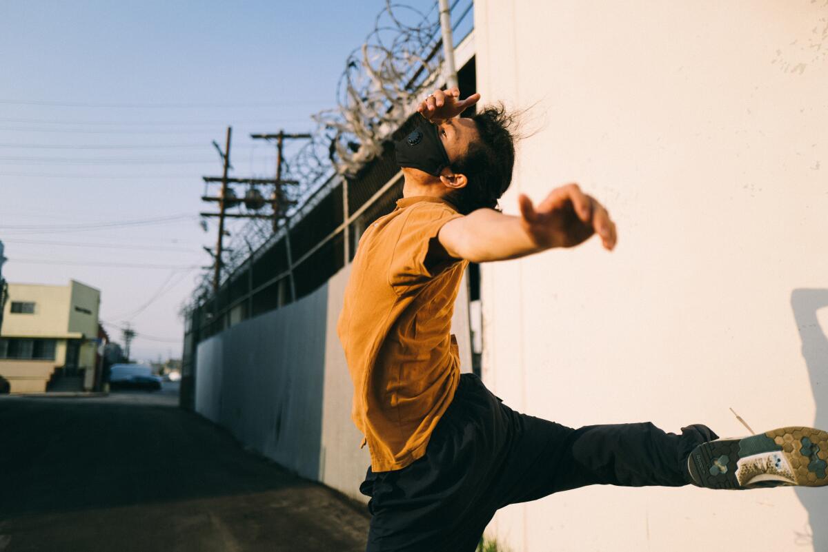 A male dancer performers in a parking lot against an industrial backdrop