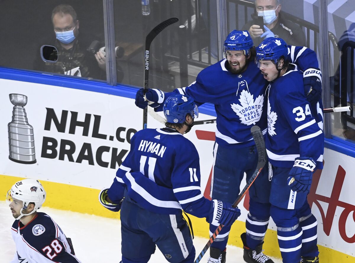 Toronto Maple Leafs center Auston Matthews (34) celebrates his goal with teammates Justin Holl (3) and Zach Hyman (11) as Columbus Blue Jackets right wing Oliver Bjorkstrand (28) skates by during second period NHL Eastern Conference Stanley Cup playoff action in Toronto on Tuesday, Aug. 4, 2020. (Nathan Denette/The Canadian Press via AP)