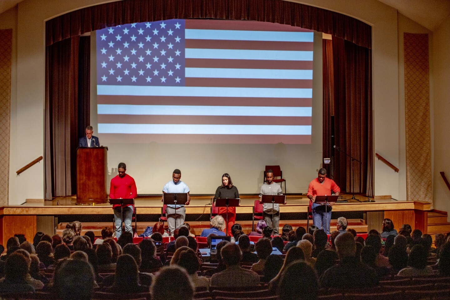 From left, Martin Kildare (at podium), Chris Mansa, Jalon Matthews, Anica Garcia-DeGraff, Malik Proctor and Fox Worth perform the stories of asylum seekers who were detained in Orange County as part of the staged reading, "Asylum Anguish: Stories from the Border." The performance concluded with a display of the American flag.