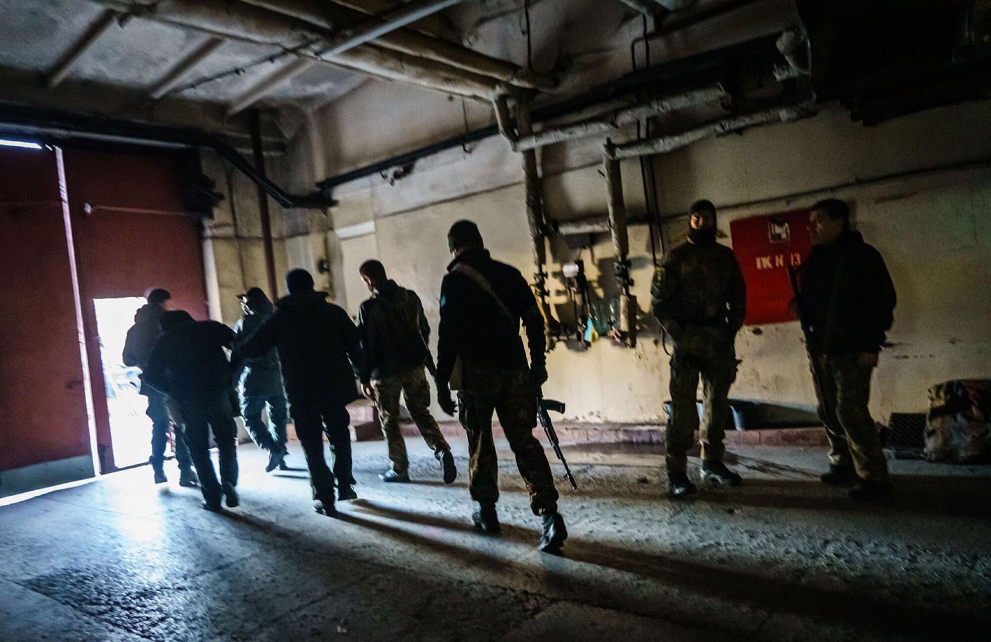 A group of armed people walk toward the open door of a building.