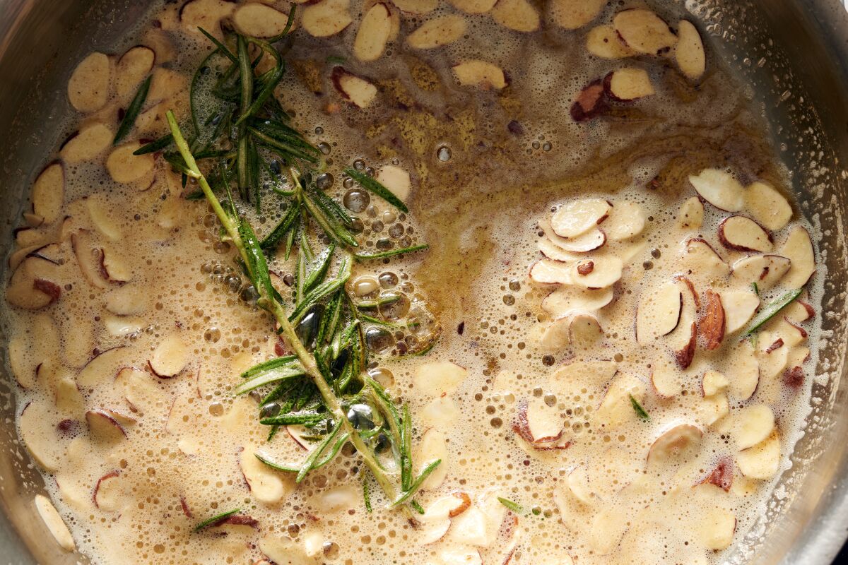 Sliced almonds cook with sprigs of rosemary in preparation for a dish of Buttery Lemon Pasta With Almonds and Arugula.
