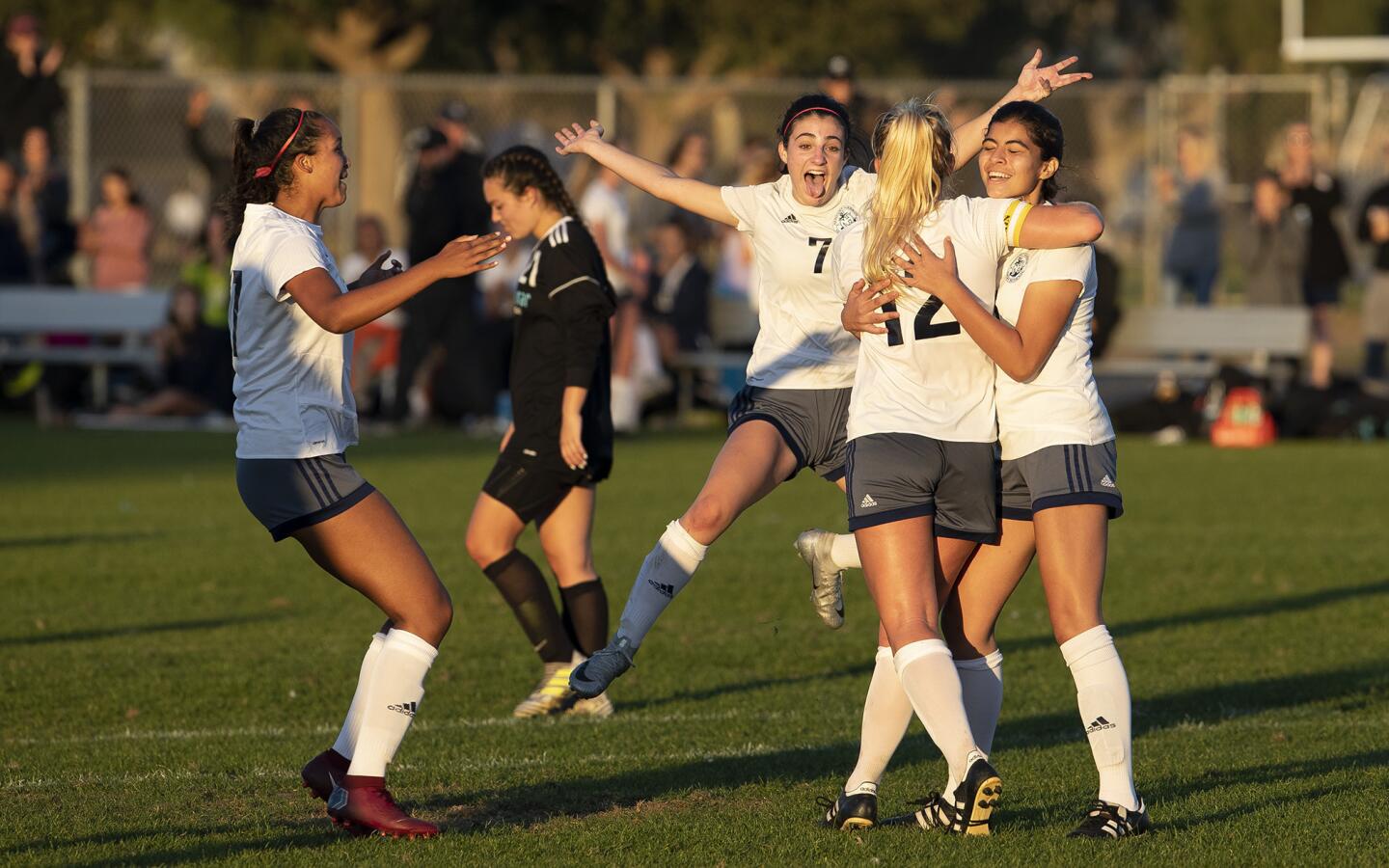 Newport Harbor's Alyssa Sims, left, Sadie Pitchess, center, and Gigt Davila, right, congratulate Emily Johnson (12) after she scored a goal on a penalty in the second half during the Battle of the Bay rivalry match against Corona del Mar on Thursday, December 20.