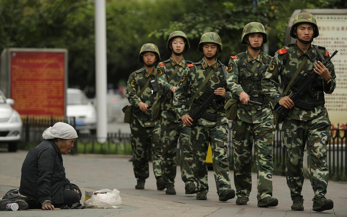 A Muslim Uighur woman begs as armed Chinese paramilitary policemen march past on a street in Urumqi on July 5, 2010.