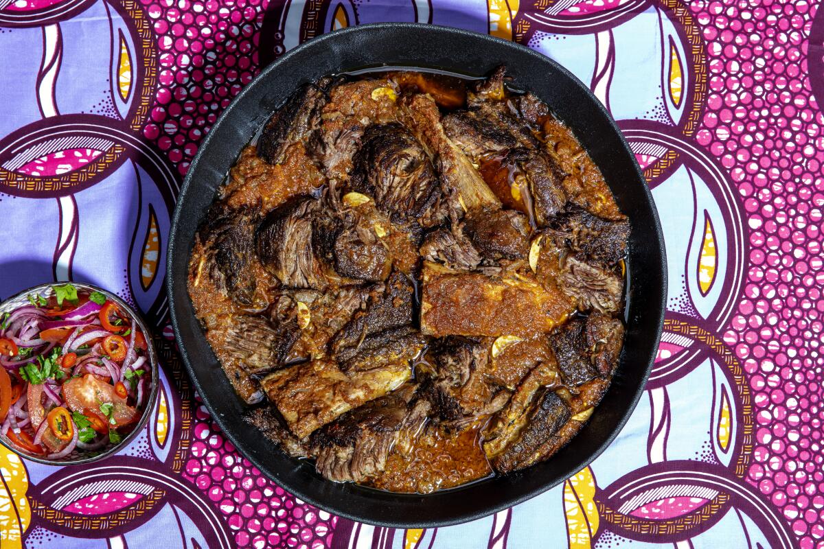 A black dish containing Beef Short Ribs in Tomato and Red Pepper Stew on a colorful tablecloth