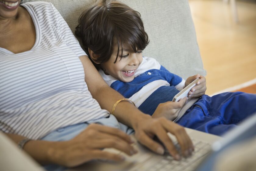 A mother and son sit side-by-side using portable screens. A recent study indicates that parents spend about as much time plugged in to screens as their kids do.