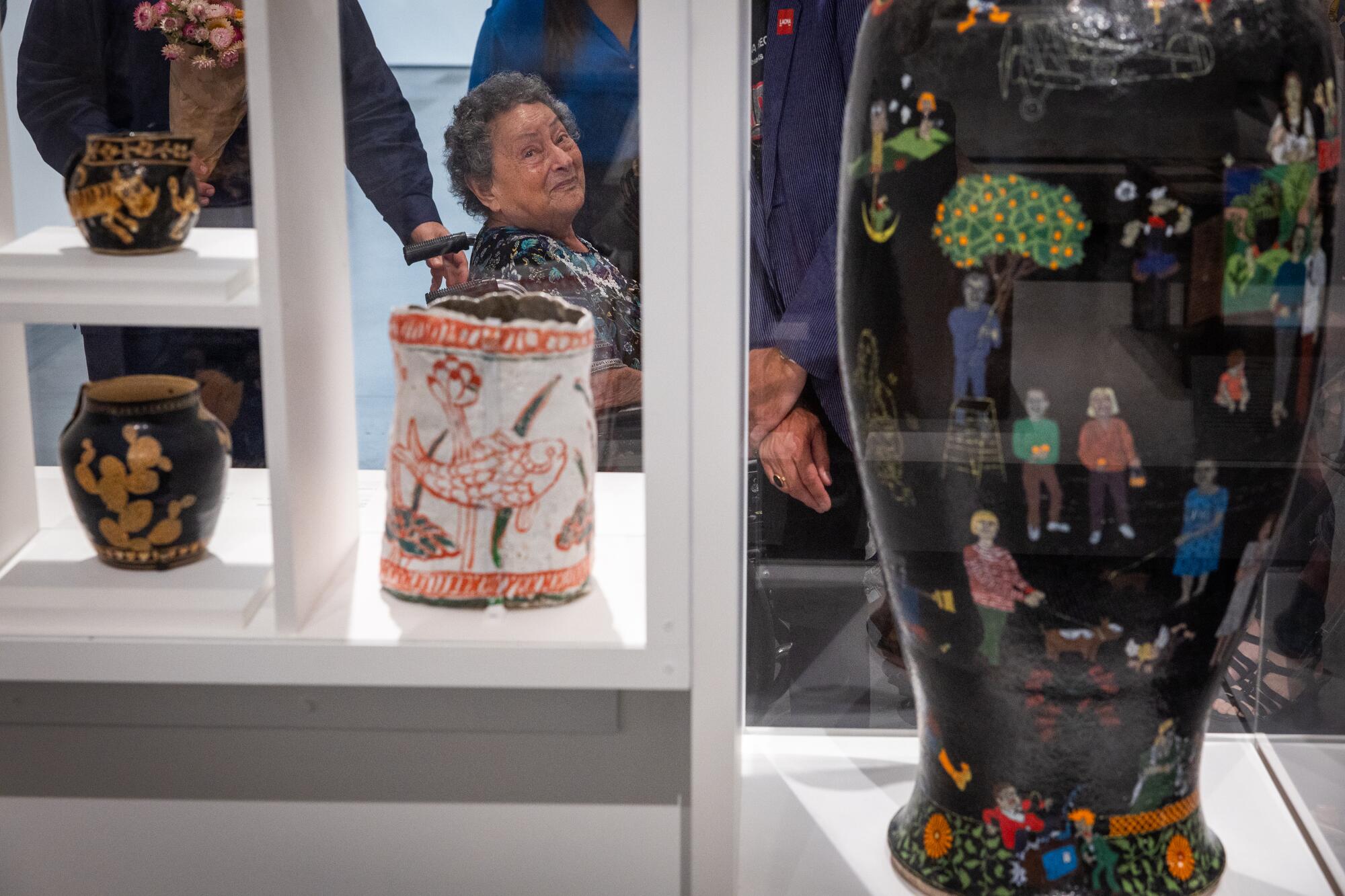 A woman in a wheelchair rolls past some of her painted ceramics at a museum.