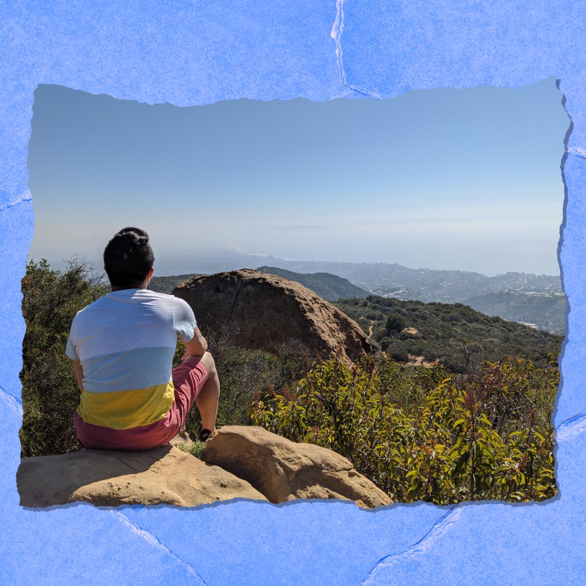 A man sits on a rock overlooking hills.