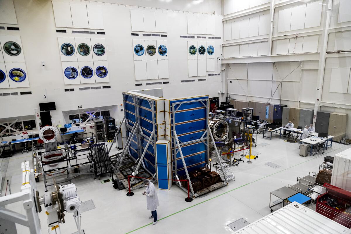 Scientists in lab coats work among equipment in a clean, well-lighted indoor space