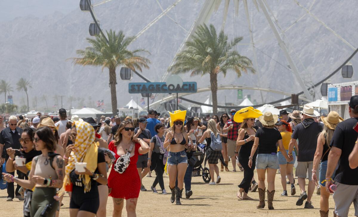 Thousands of country music fans arrive at Stagecoach. There are palm trees, a Ferris wheel and mountains in the background.