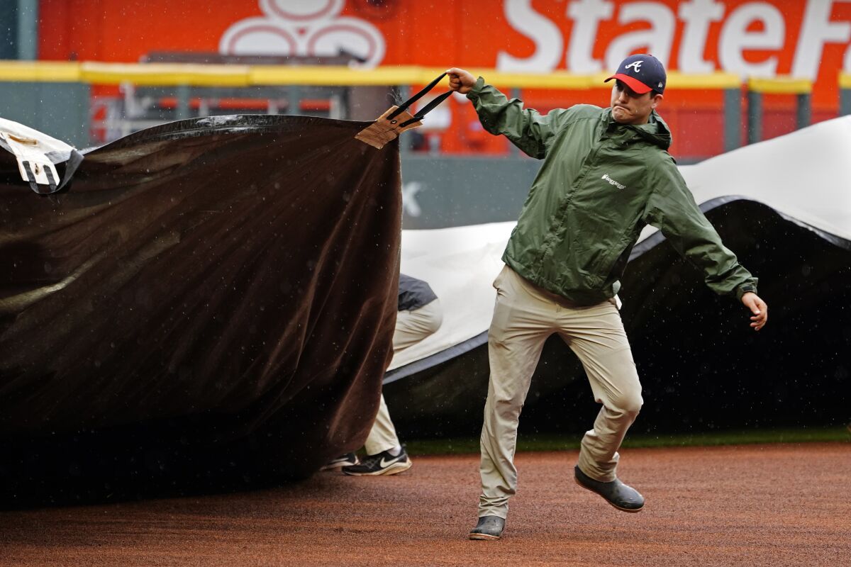 Members of the Atlanta Braves grounds crew work to cover the infield before a baseball game between Atlanta Braves and Colorado Rockies was cancelled because of rain Thursday, Sept. 16, 2021, in Atlanta. (AP Photo/John Bazemore)
