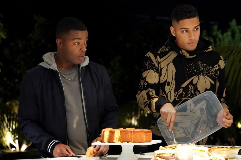 Two young men at a table with cake and sandwiches.