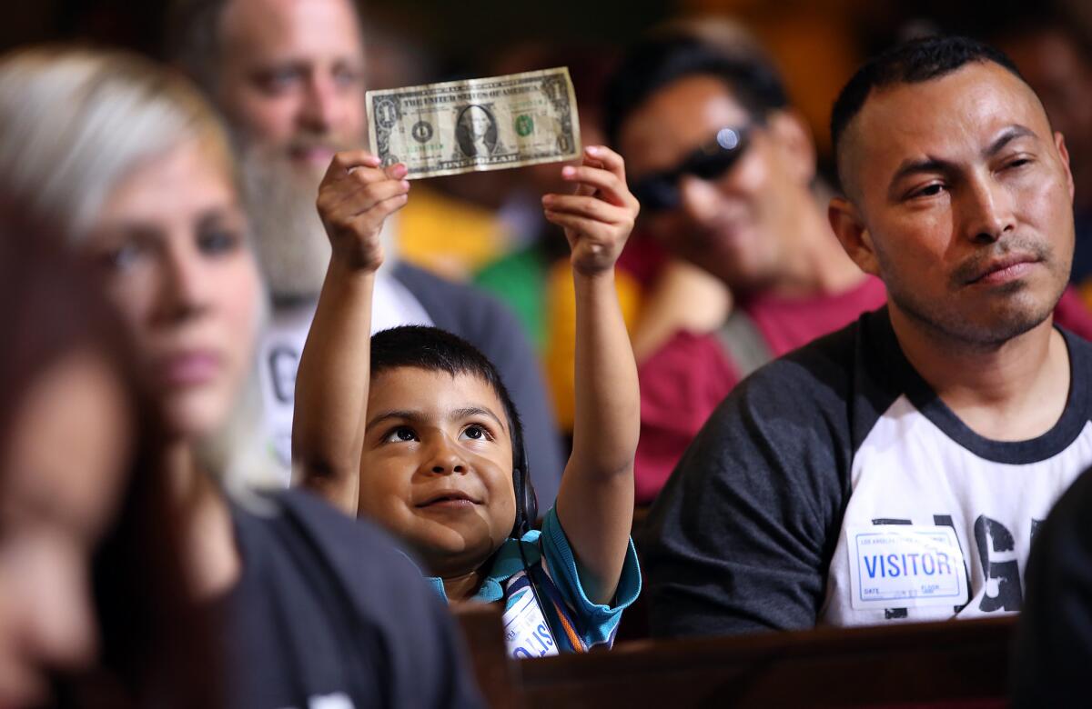 David Lazo, 5, holds a dollar bill as his father, Francisco, watches the City Council debate on raising the minimum wage on June 3. The panel voted to raise the minimum wage to $15 an hour by 2020.