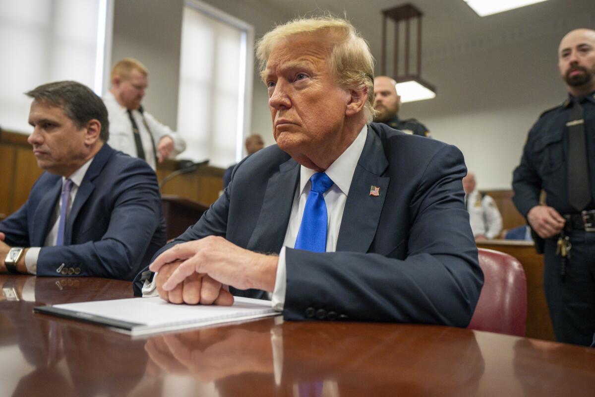 Former President Trump sits at a table in a courtroom.