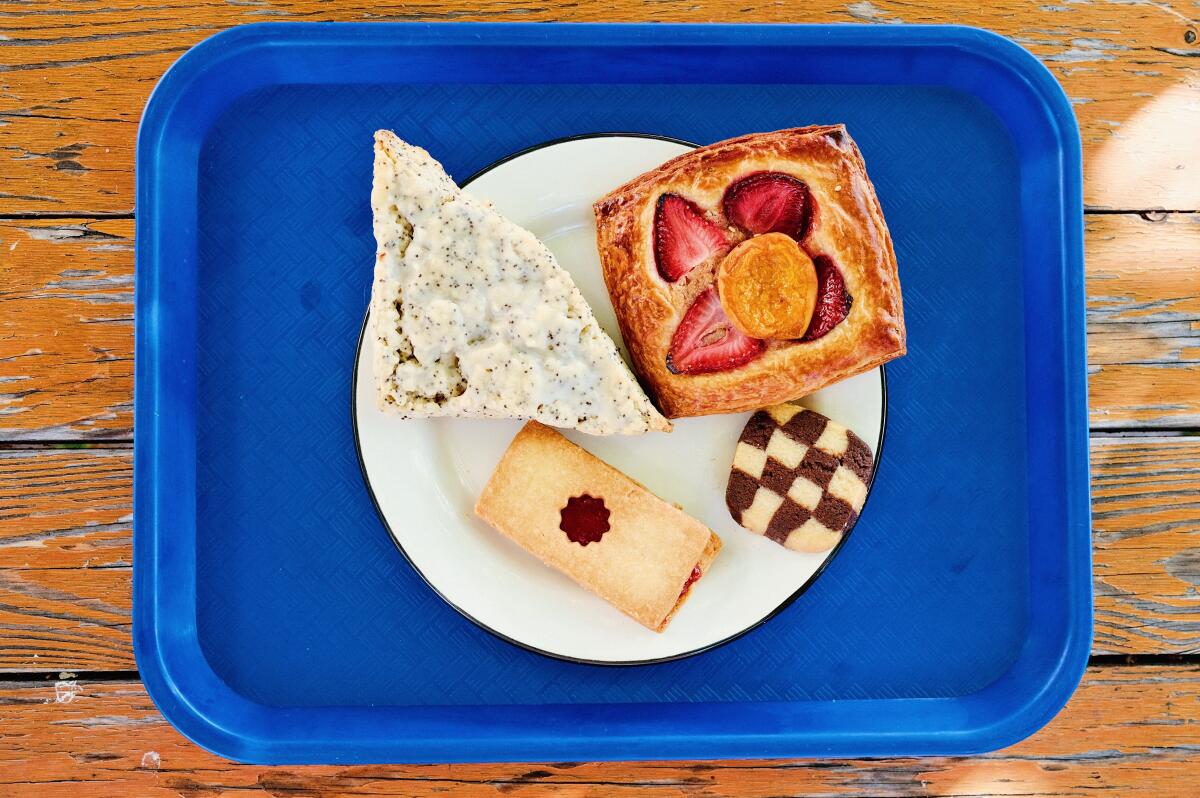 An overhead of assorted pastries on a blue tray from Baker's Bench bakery: a strawberry croissant, cookies and a scone.