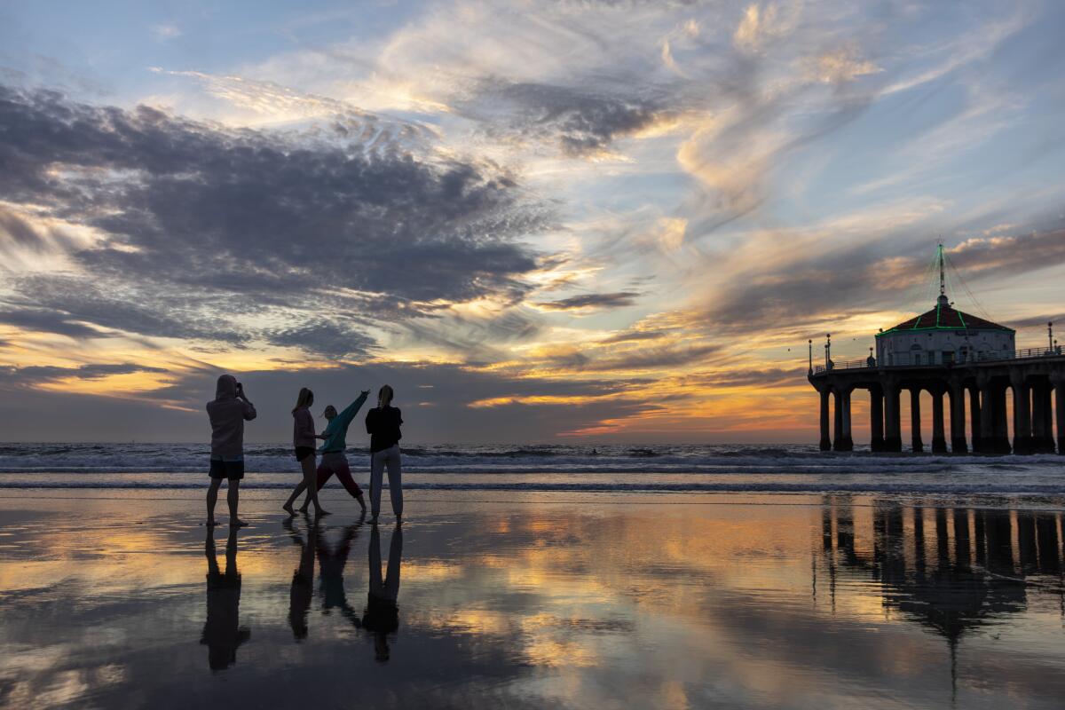 People silhouetted by the sunset at a beach with a pier