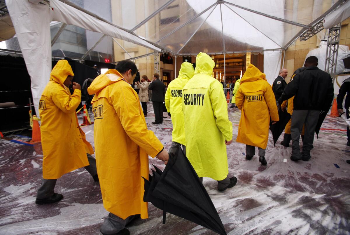 Security personnel wear rain gear outside the Dolby Theater at Hollywood and Highland, where rehearsals and preparations continue for the Oscars.