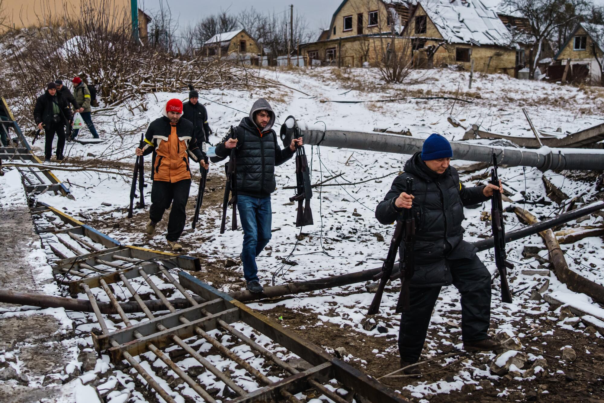 Volunteers carry rifles across a river under a destroyed bridge to reinforce Ukrainian troops in Irpin, Ukraine