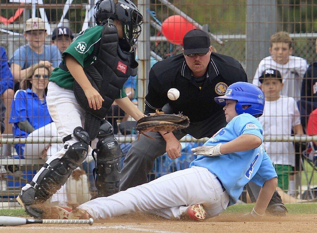 Earthpack's Connor McGuire, right, slides safely into home plate as Dick's Sporting Goods catcher Steven McMillen, left, bobbles the ball during the Newport Beach Little League majors division championship game at Lincoln Elementary on Saturday.