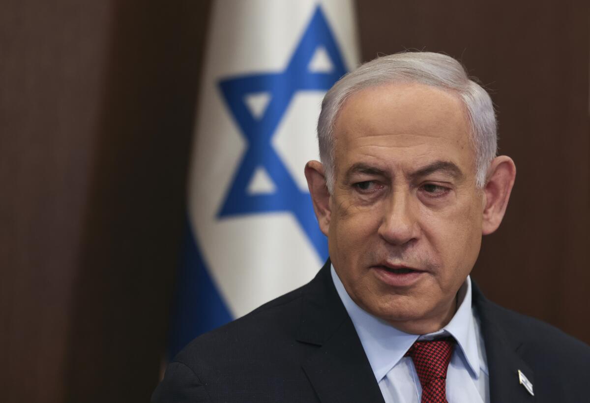 Israeli Prime Minister Benjamin Netanyahu in a suit in front of a flag.
