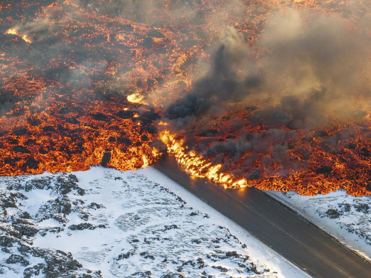 An aerial view of lava flowing onto a road amid a snowy landscape.