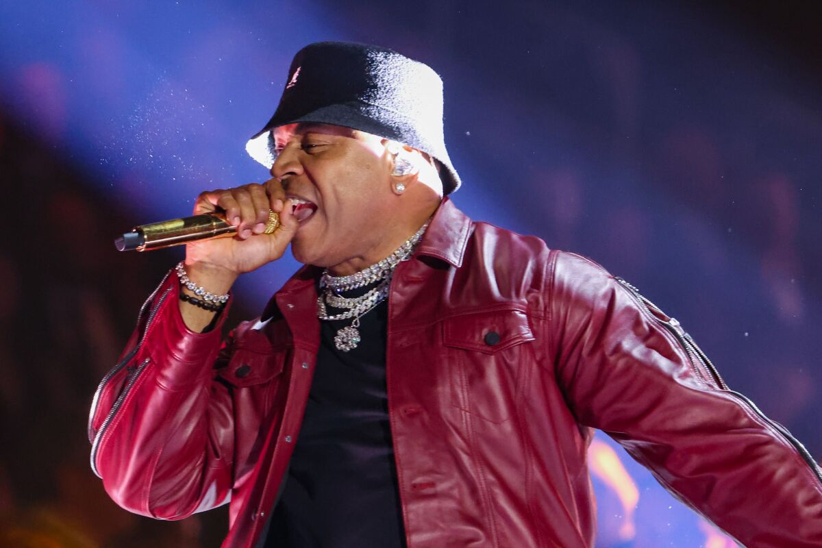 A man in a red leather jacker and black bucket hat performing with mic to his mouth during awards show.