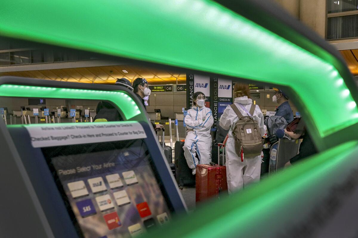 A few travelers wear biohazard suits and masks at Tom Bradley International Terminal at LAX