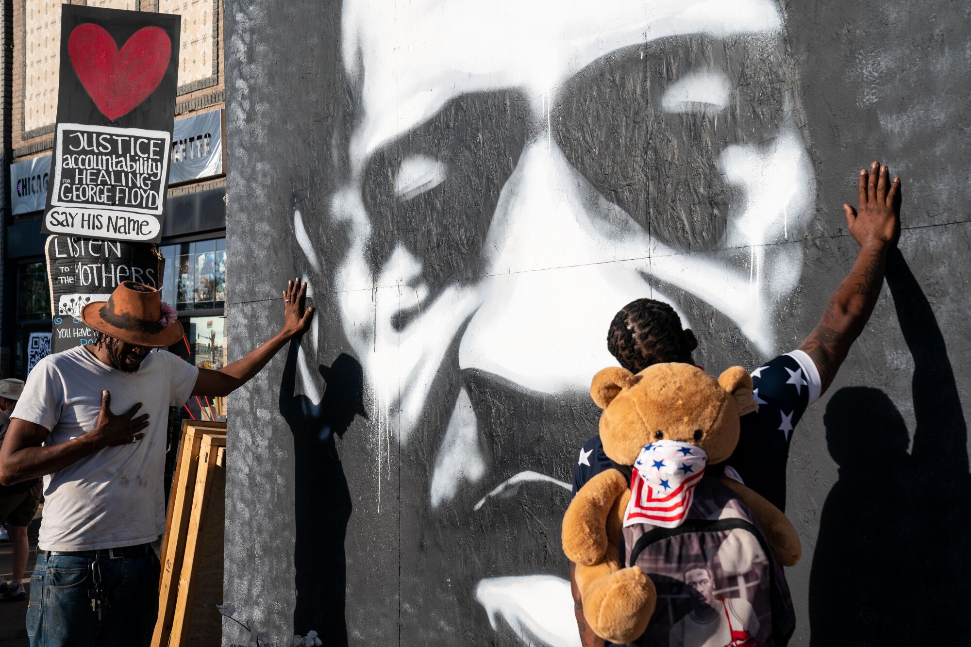 Two Black men place their hands on a mural depicting George Floyd