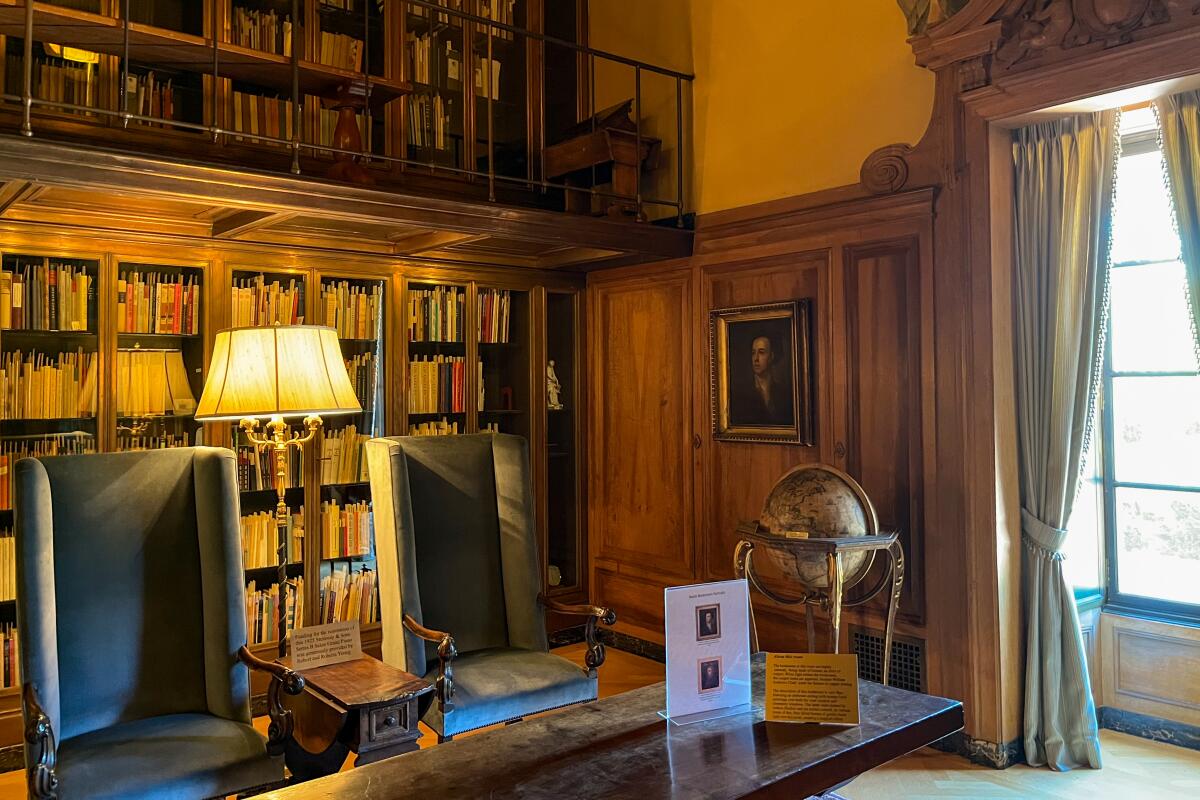 A corner of a library featuring a globe, a window with long drapes, and shelves of books with a lamp.