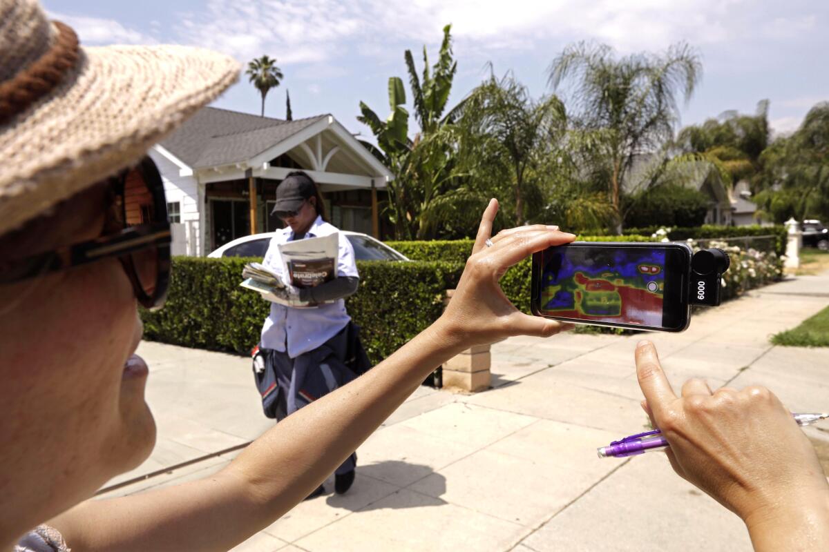 A woman takes a thermal photograph as a mail carrier walks in the background