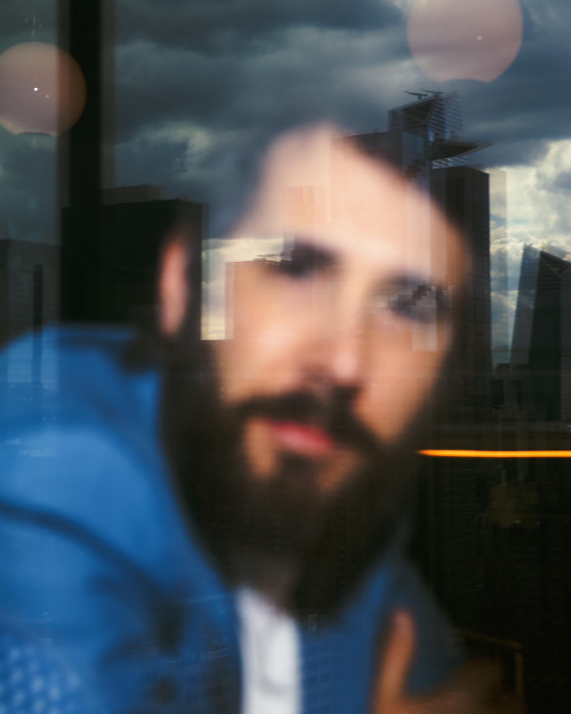 A blurry shot of a heavily bearded Josh Groban looking out a window.
