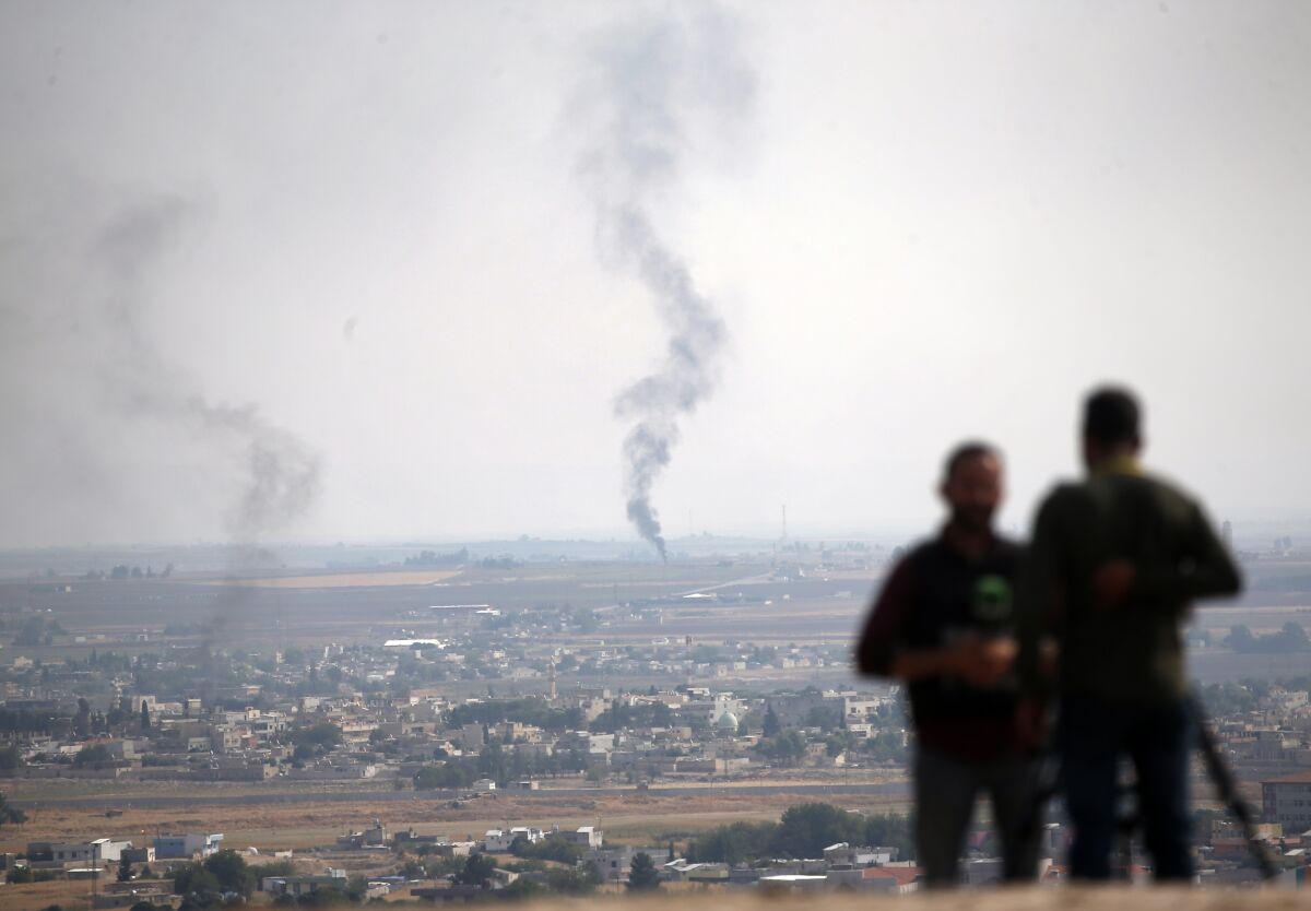 Television journalists work on a hilltop in Ceylanpinar, southeastern Turkey, with smoke billowing from a fire in Ras al-Ayn, Syria, serving as the backdrop on Oct. 20, 2019.