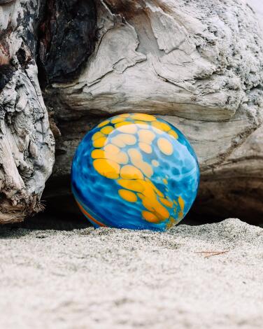 A colorful glass float tucked among large rocks on a beach