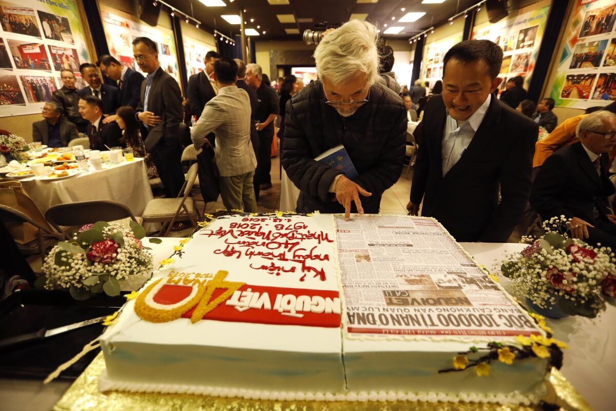 Tai Do, center, and Steven Mai look over a cake featuring the front page of the first issue of Nguoi Viet Daily News during the 40th anniversary celebration of the paper in Westminster. (Genaro Molina / Los Angeles Times)