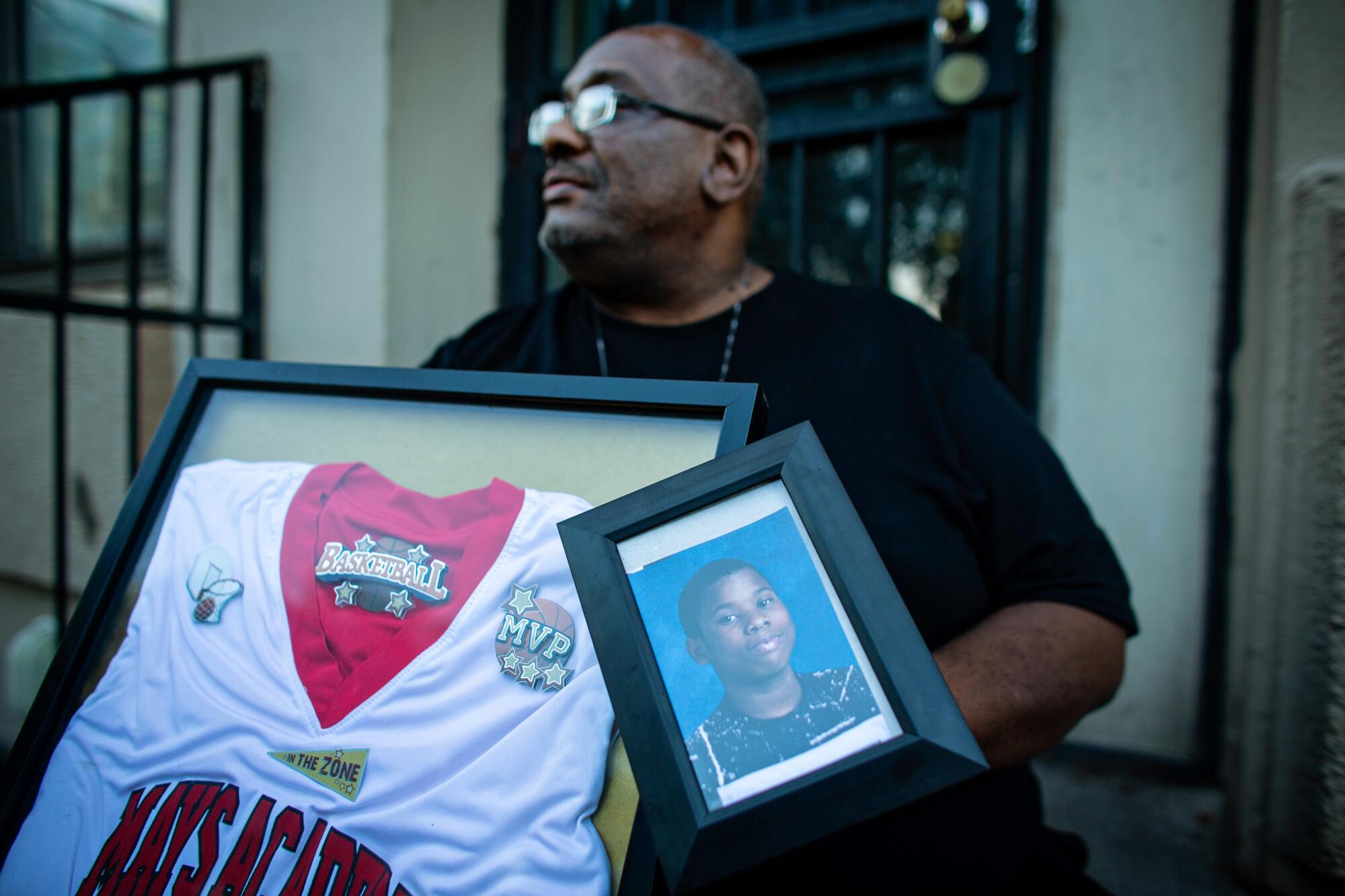 Donald Williams sits on the stoop of his home holding a photo and basketball jersey of his late son Deon Williams