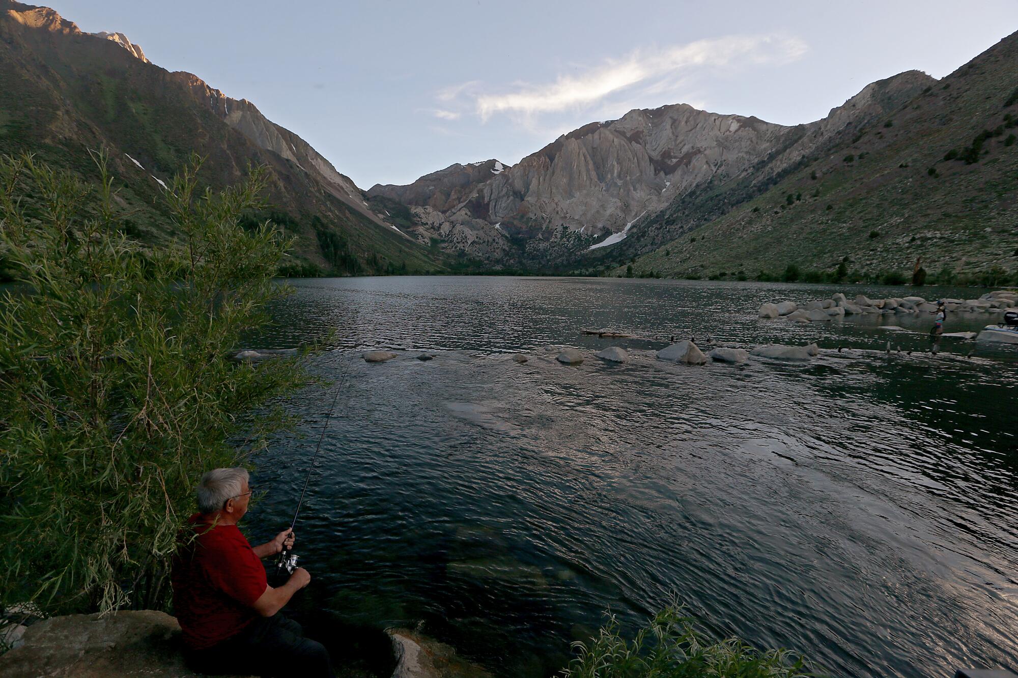 A man casts a fishing line into a mountain lake. 