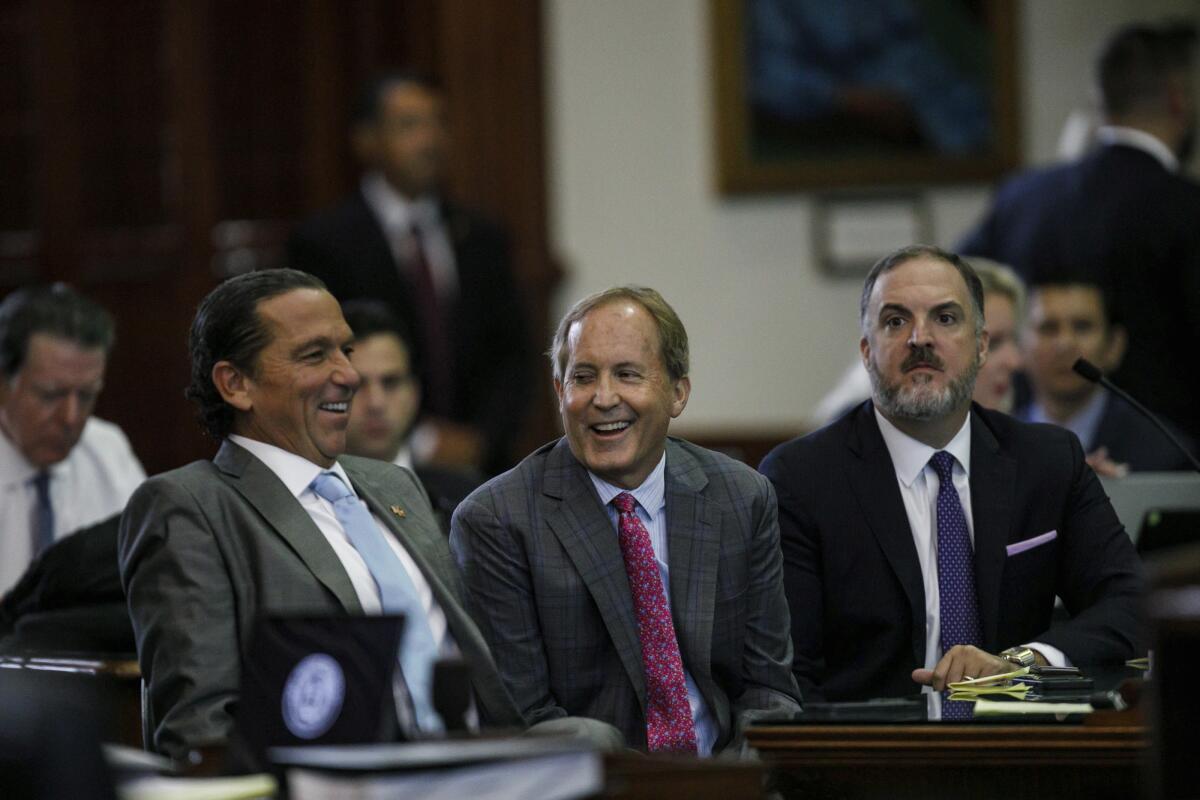 Ken Paxton smiles as he sits between defense attorneys.