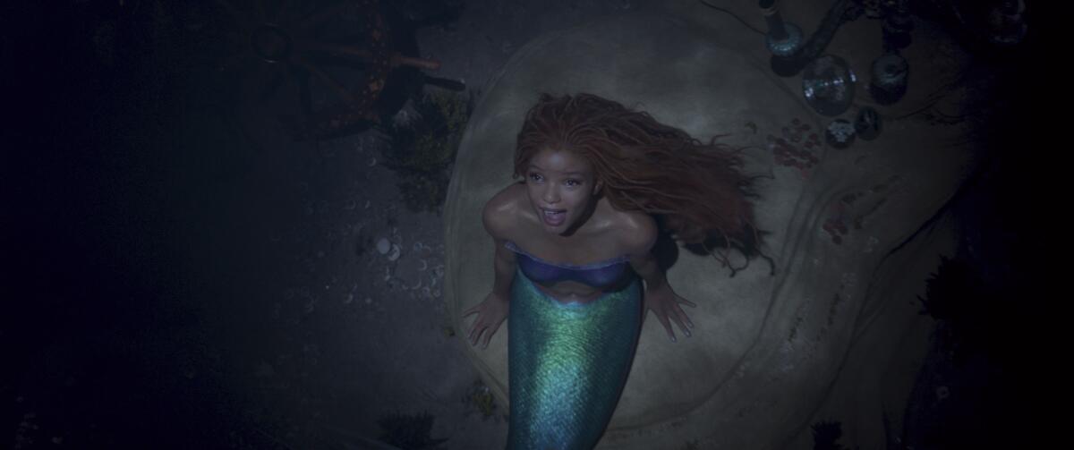 Halle Bailey, dressed as a mermaid, sings underwater while sitting on a rock.