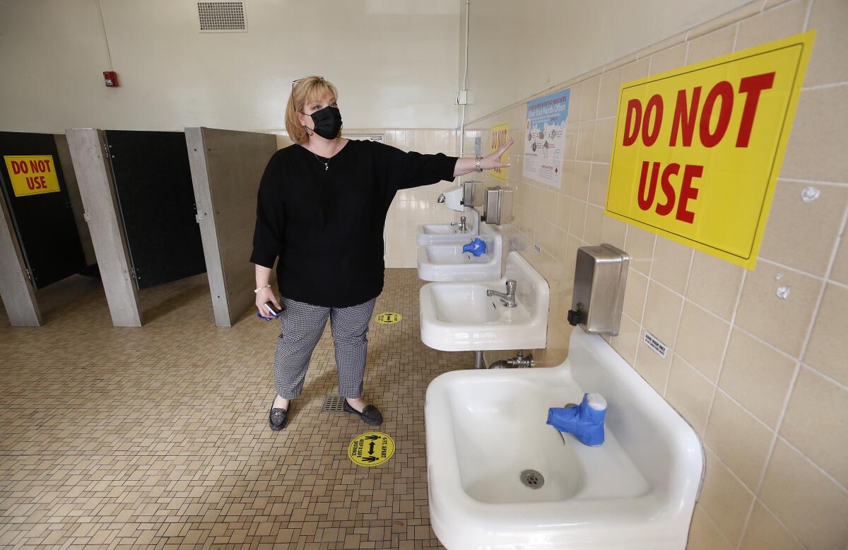 An elementary school principal points to taped-off sinks and closed stalls in a school bathroom.