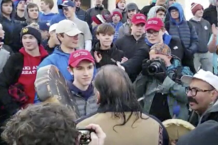 In this Friday, Jan. 18, 2019 image made from video provided by the Survival Media Agency, a teenager wearing a "Make America Great Again" hat, center left, stands in front of an elderly Native American singing and playing a drum in Washington. The Roman Catholic Diocese of Covington in Kentucky is looking into this and other videos that show youths, possibly from the diocese's all-male Covington Catholic High School, mocking Native Americans at a rally in Washington. (Survival Media Agency via AP)