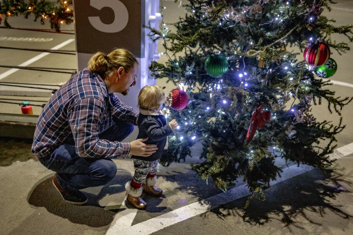 Una niña de 13 meses se interesa por el árbol de Navidad en compañía de su padre.