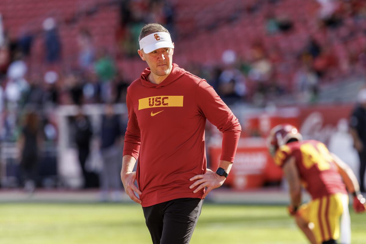 USC coach Lincoln Riley stands with his hand on his hips as players warm up before a game.