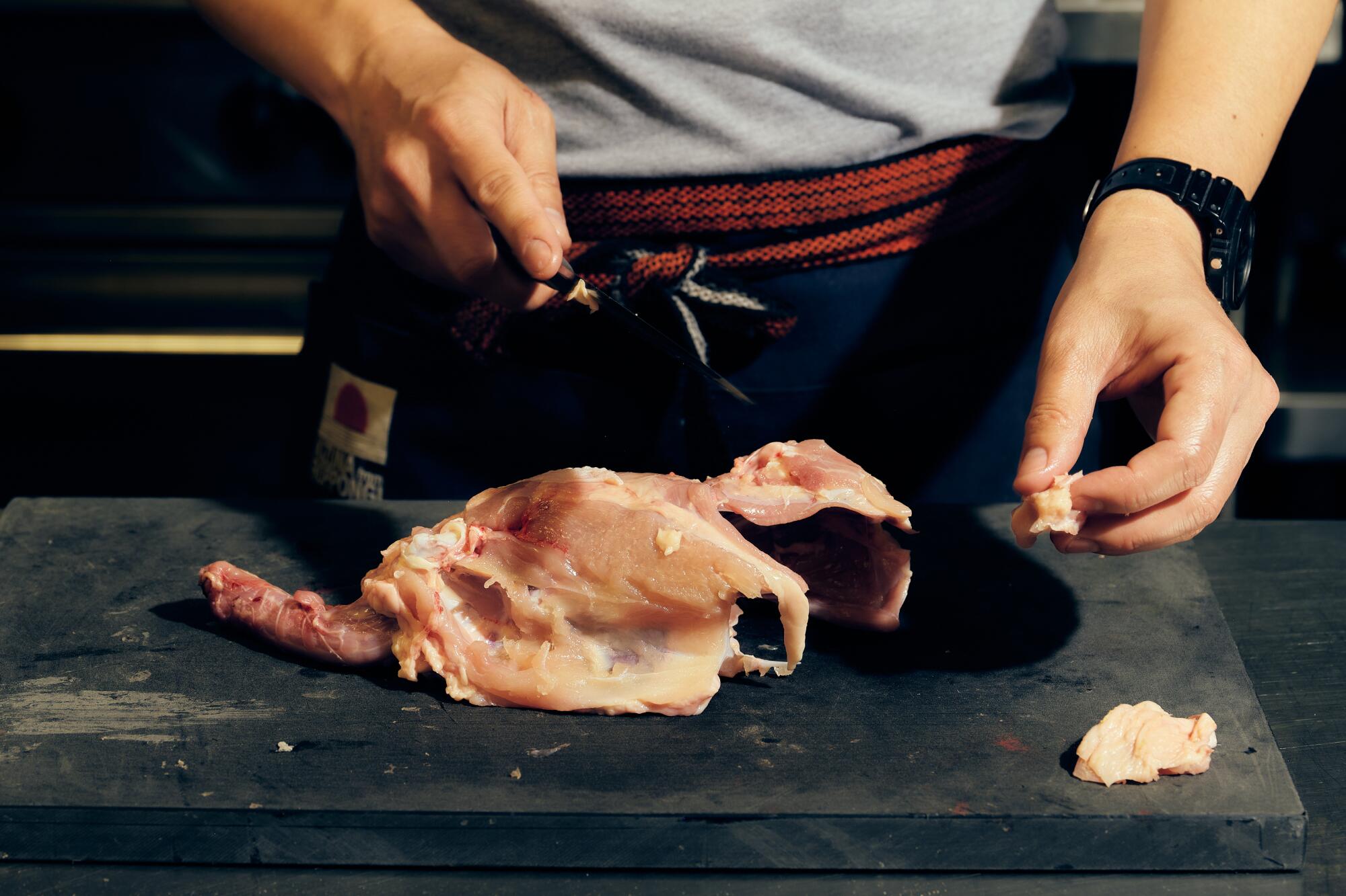 Hands at work cutting raw chicken.