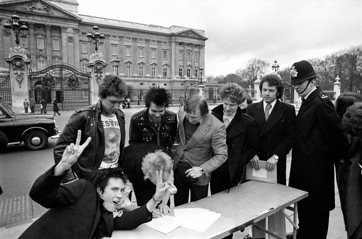 Members of the Sex Pistols sign a contract on a folding table outside Buckingham Palace