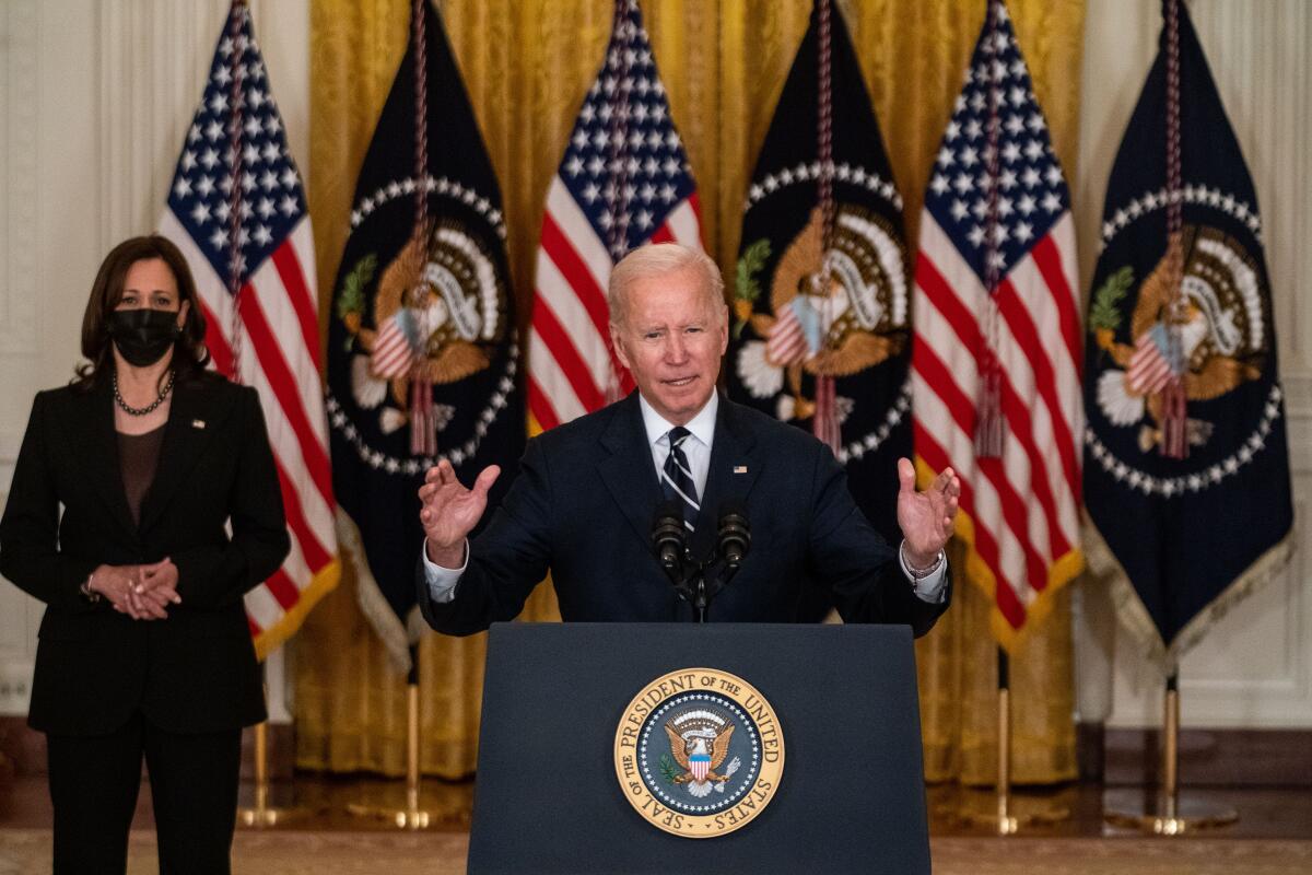 President Biden stands in front of flags as he speaks at a podium. Kamala Harris stands behind him.