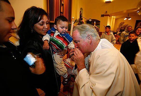 Father Peter Banks kisses the hand of a young parishioner at St. Lawrence of Brindisi Church in Watts